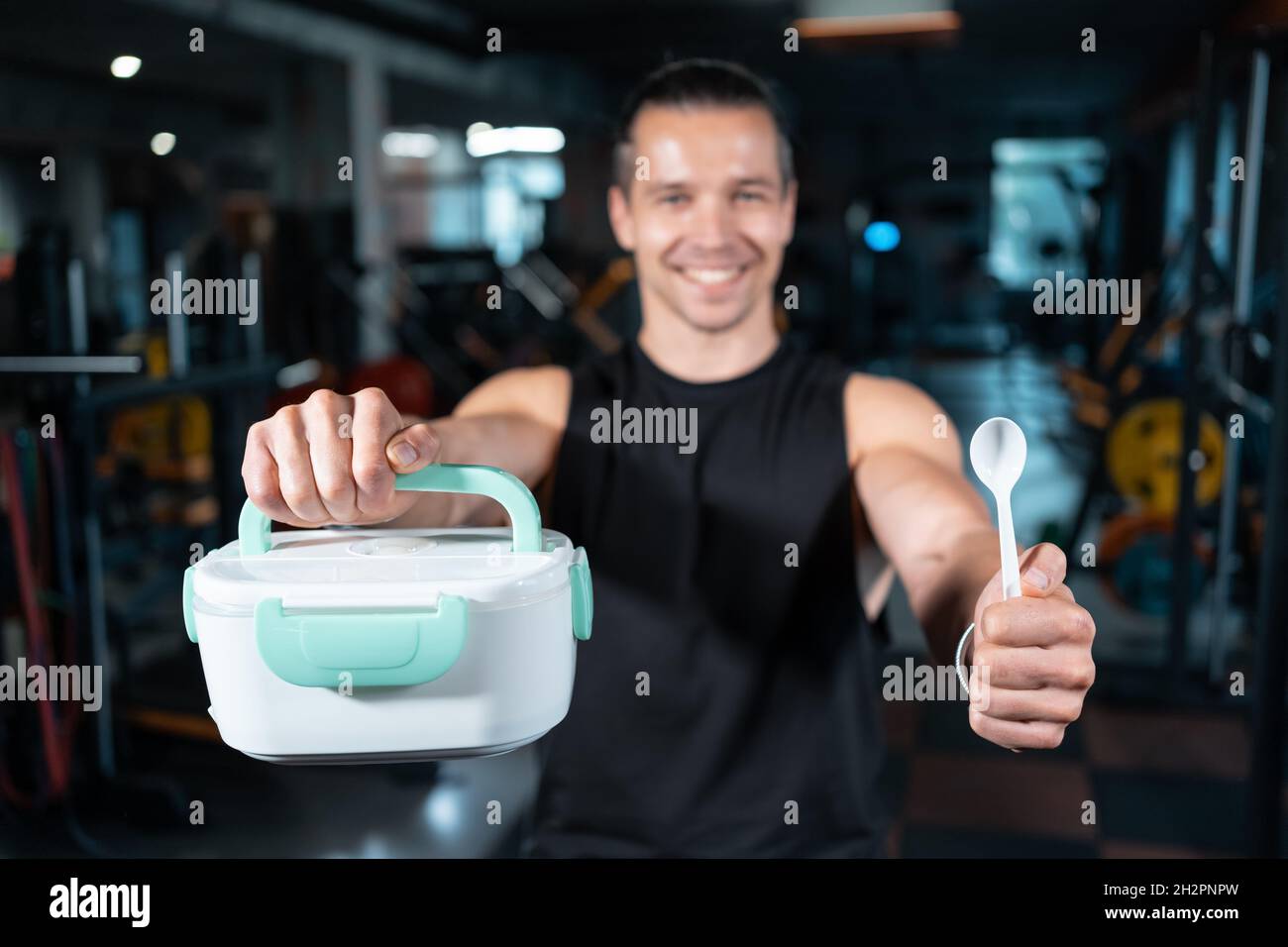 young attractive man personal trainer holding lunch box with breakfast in gym Stock Photo