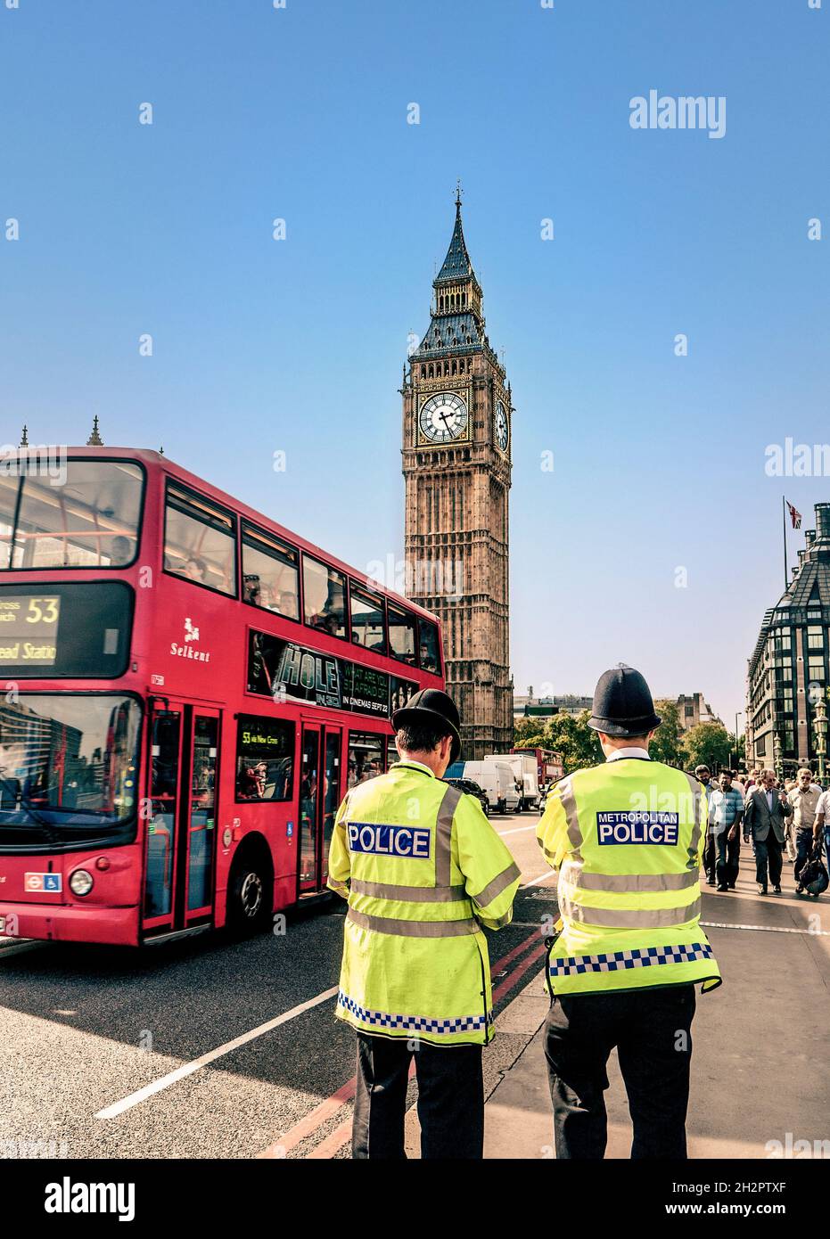 London Metropolitan Police officers wearing helmets and high visibility jackets on Westminster Bridge street security duty back view with red london bus at Westminster Bridge Houses of Parliament London UK Stock Photo