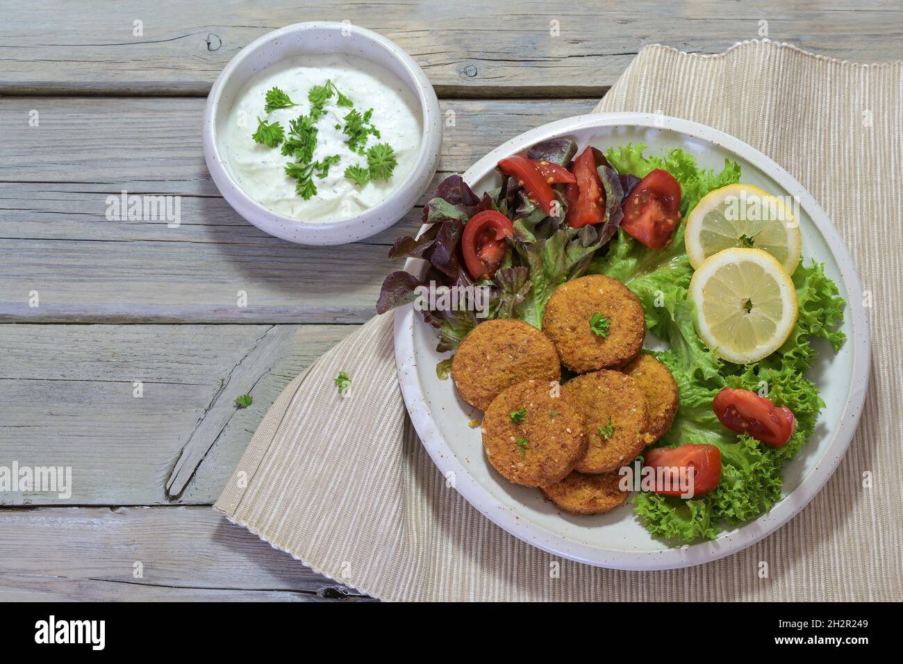 Vegetarian falafel with salad on a plate and yogurt dip in a bowl on a rustic gray wooden table, copy space, high angle view from above, selected focu Stock Photo