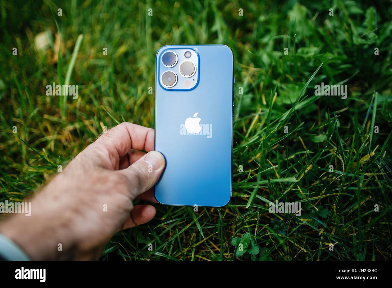 Apple Computers iPhone 13 pro with all three rear cameras and lidar sensor in green garden grass background environmentally friendly Stock Photo