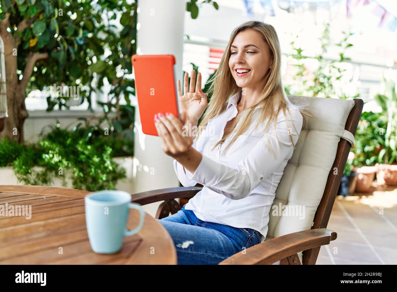 Young blonde woman smiling happy using touchpad sitting on the table at ...