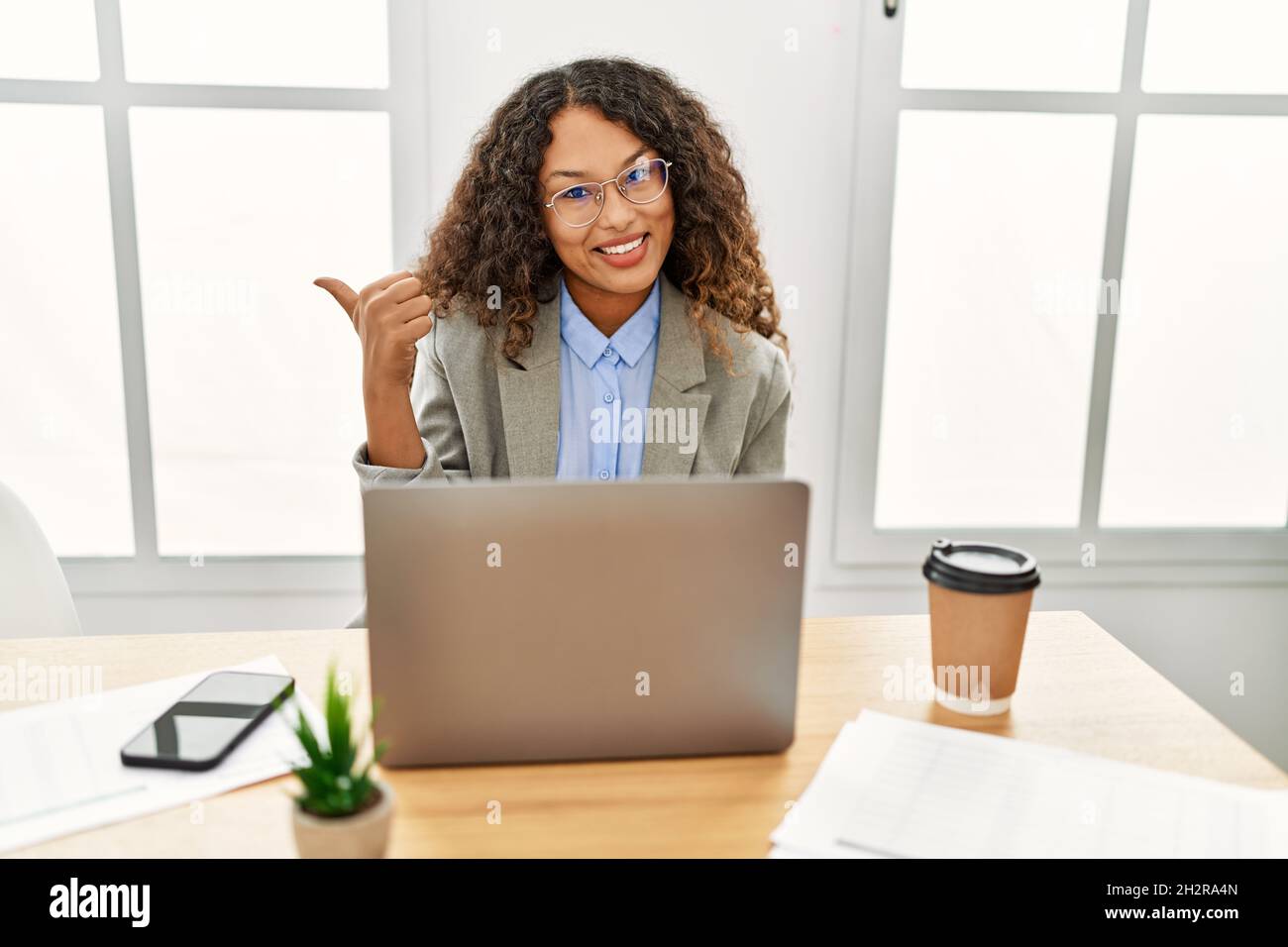 Beautiful hispanic business woman sitting on desk at office working ...