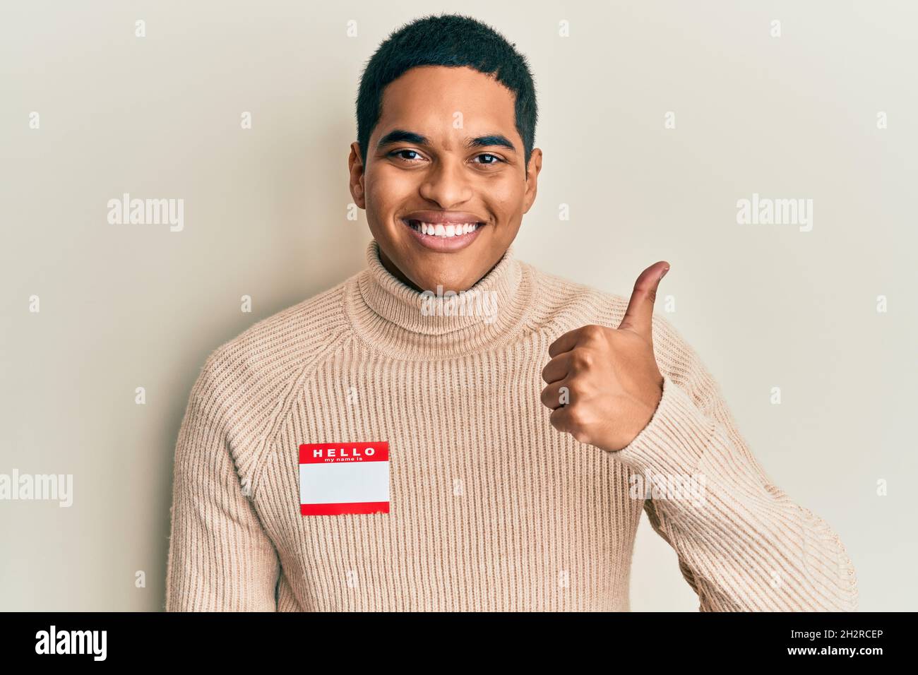 Young handsome hispanic man wearing hello my name is sticker ...