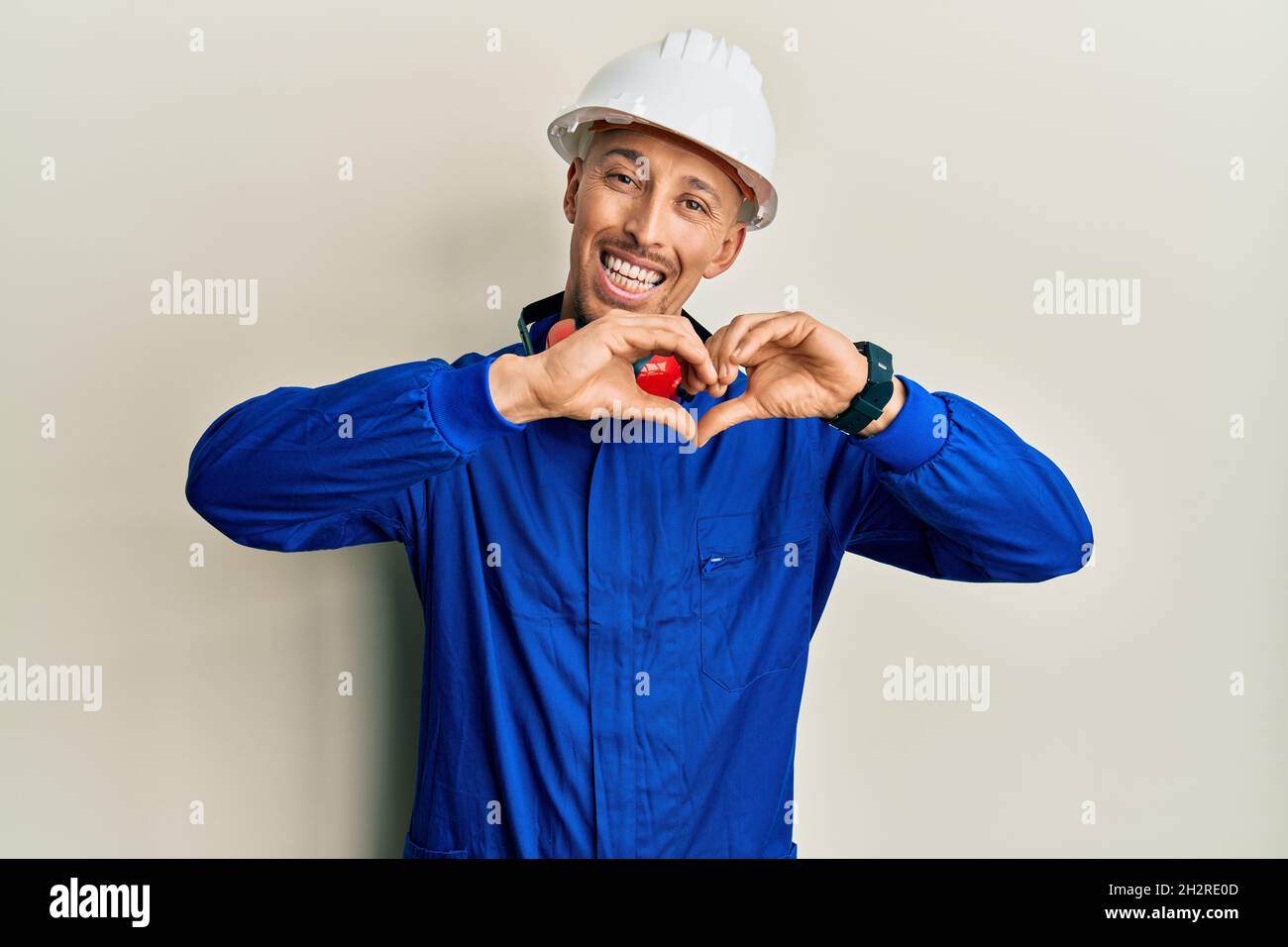 Bald man with beard wearing builder jumpsuit uniform and hardhat