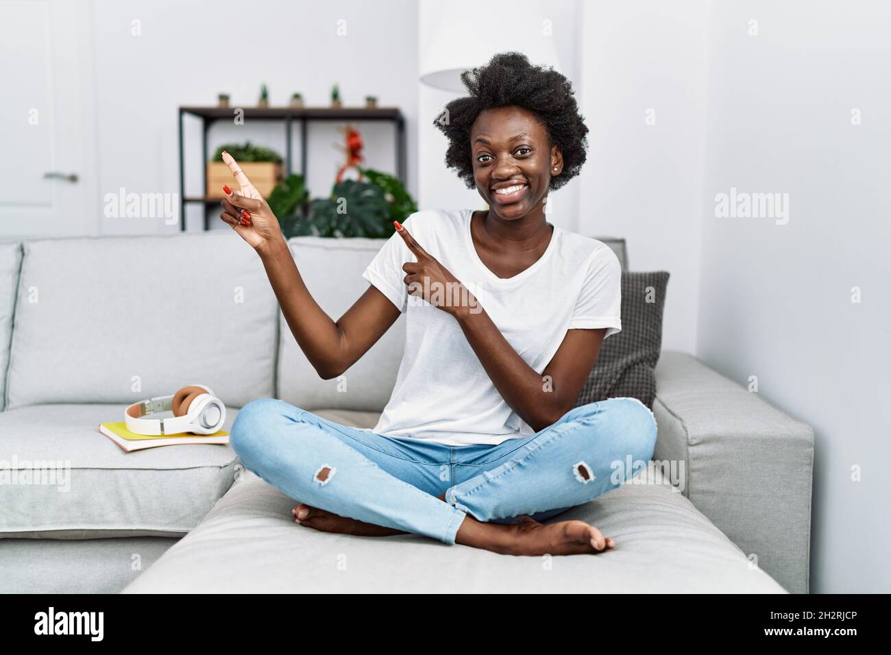 African young woman sitting on the sofa at home smiling and looking at ...