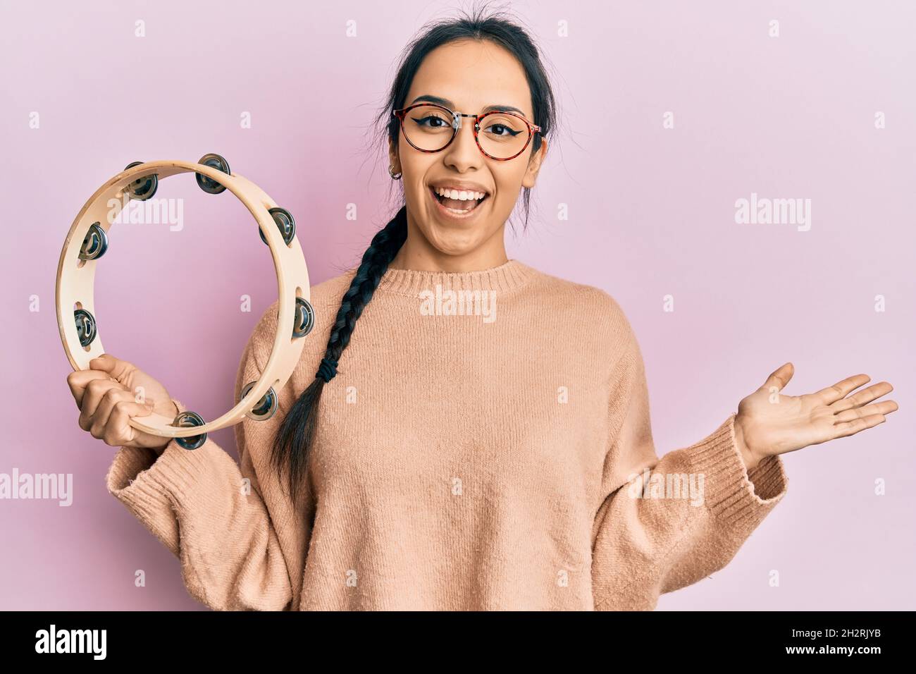 Young hispanic girl playing tambourine celebrating achievement with