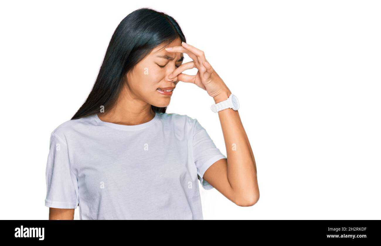 Beautiful young asian woman wearing casual white t shirt smelling something stinky and disgusting, intolerable smell, holding breath with fingers on n Stock Photo
