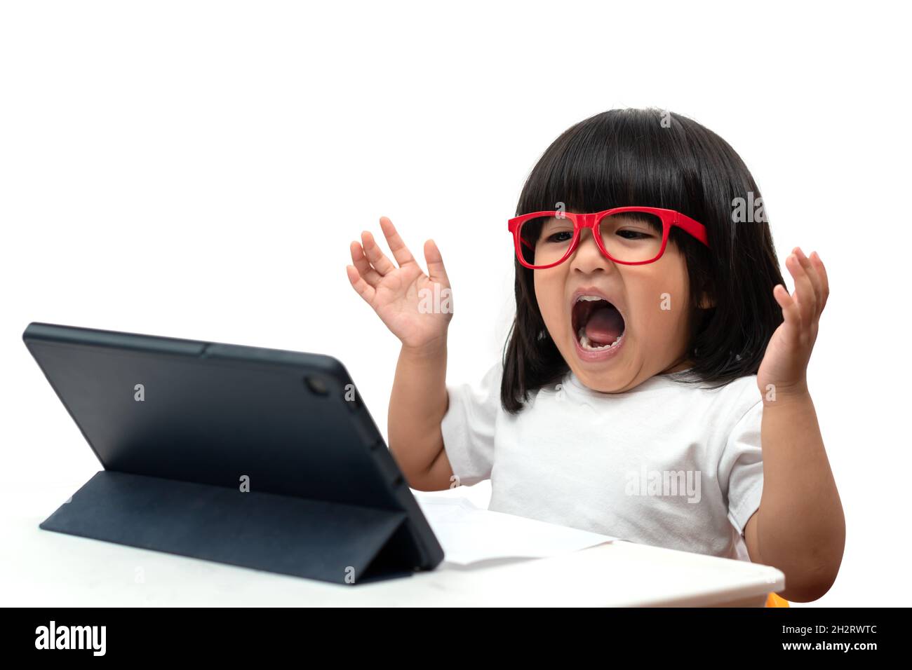 Little Asian Preschooler girl wearing red glasses and using tablet pc on white background and surprise acting, Asian girl learning with a video call w Stock Photo