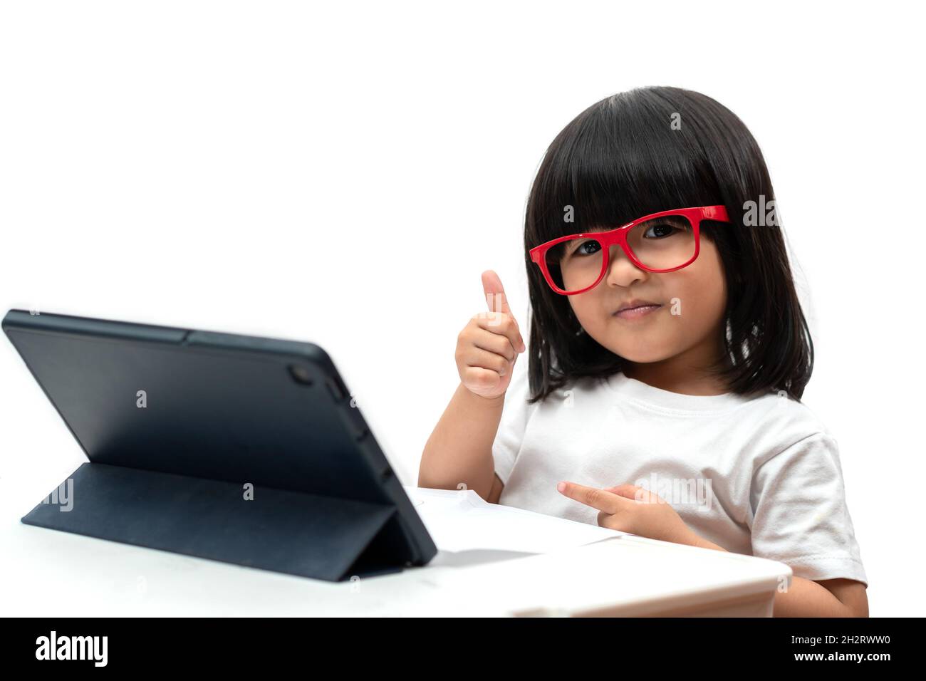 Little Asian Preschooler girl wearing red glasses and using tablet pc on white background and thumbs up, Asian girl learning with a video call with ta Stock Photo