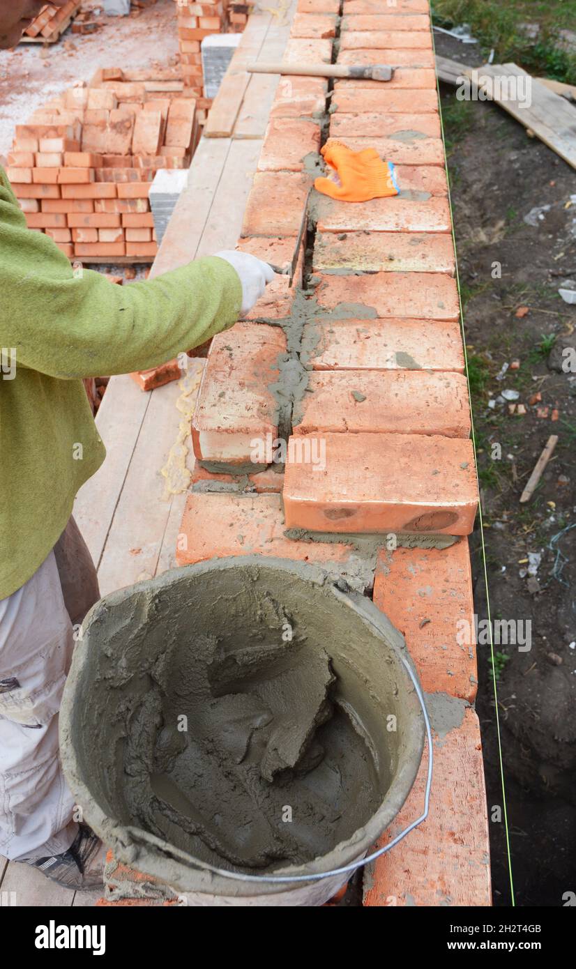 Bricklayer Worker Installing Red Blocks and Caulking Brick Masonry