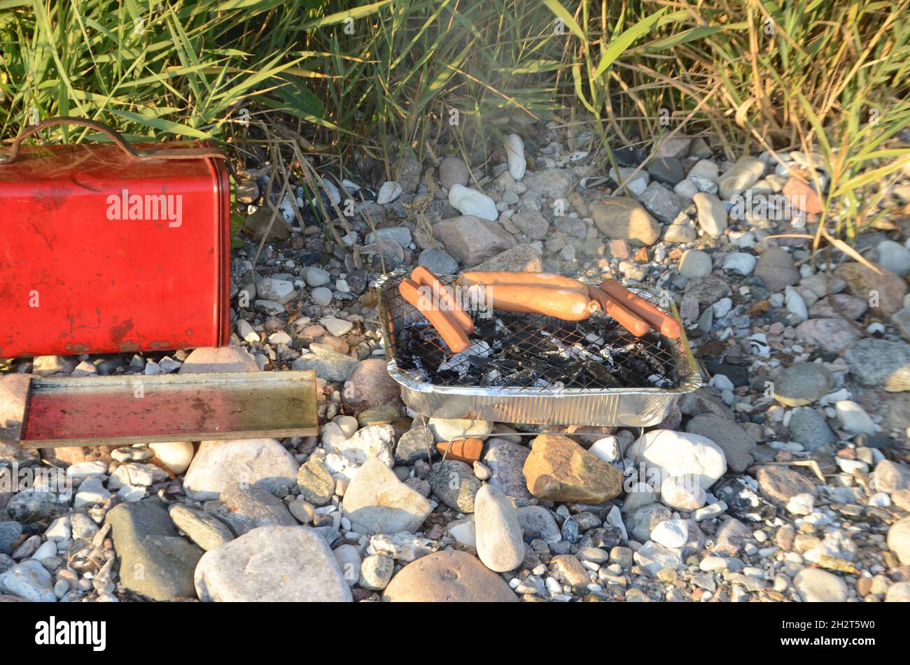 Single use BBQ with sausages on a stony shore. Stock Photo