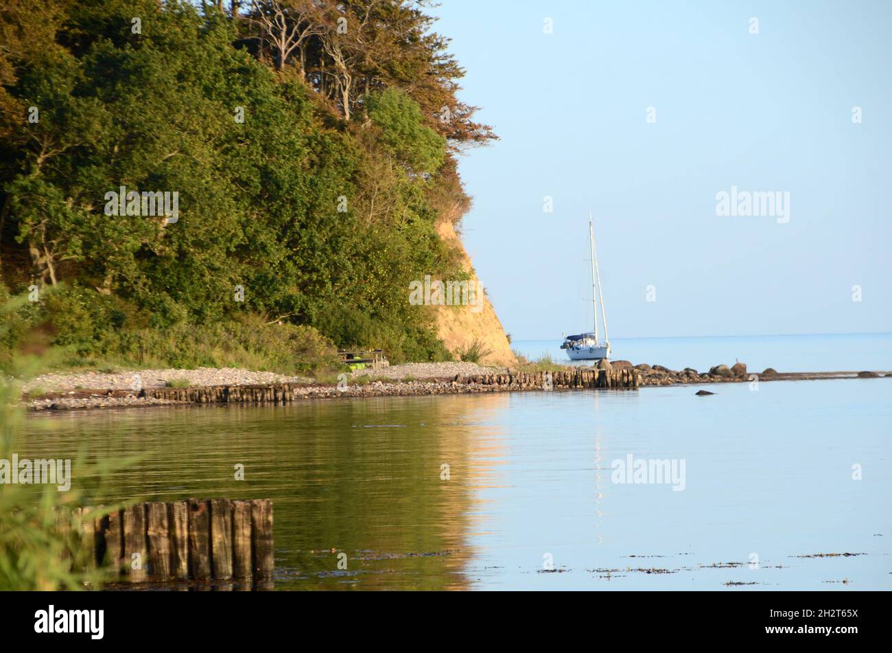 Coast part with a leisure yacht with lashed sails seen behind a point. Stock Photo