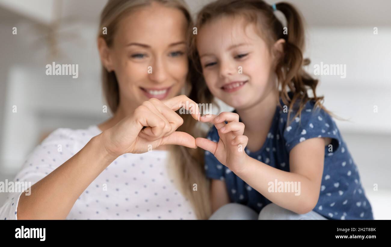 Smiling young mother and little kid daughter showing heart symbol. Stock Photo