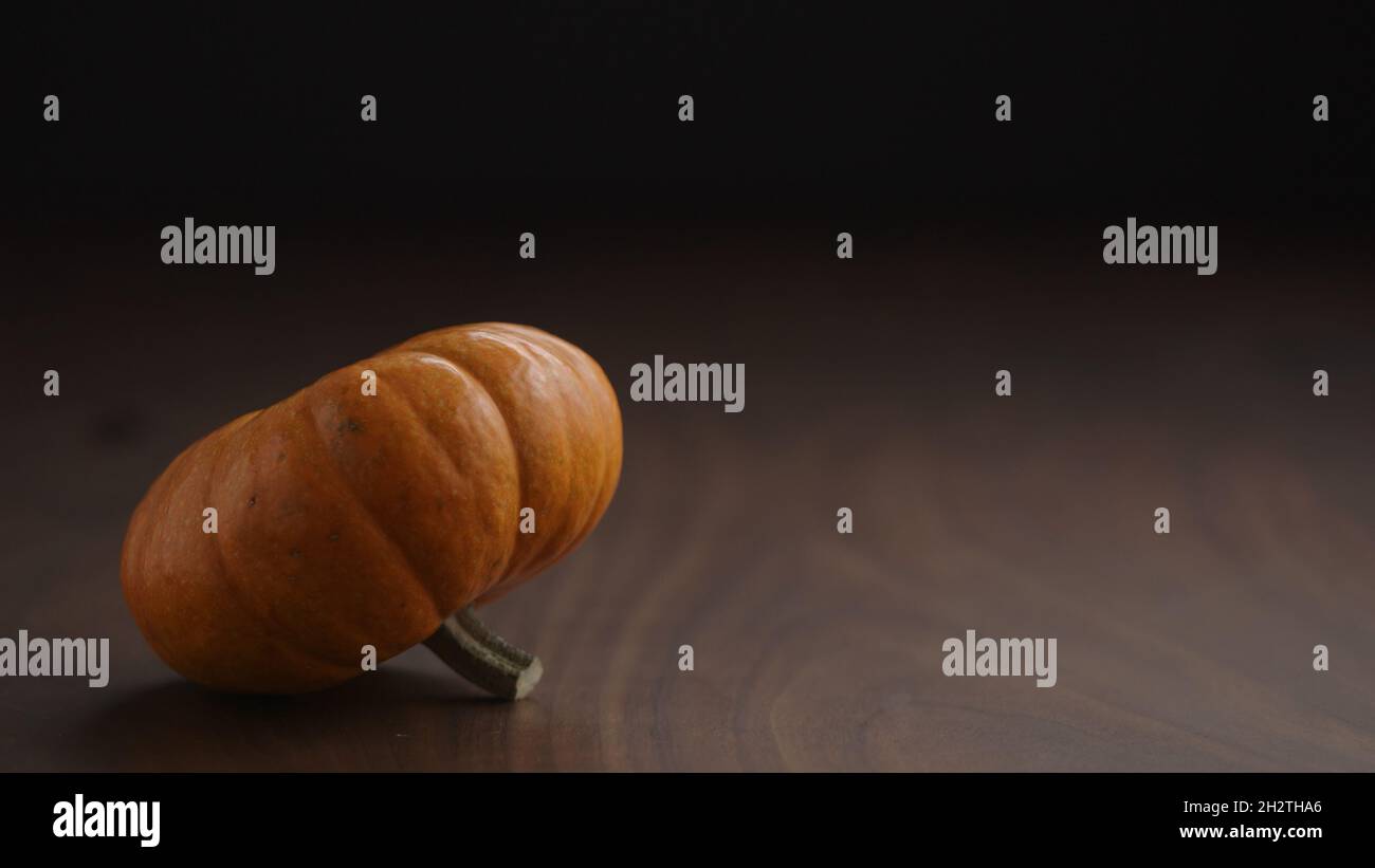 small orange pumpkin on walnut table with balck wall and , wide photo ...