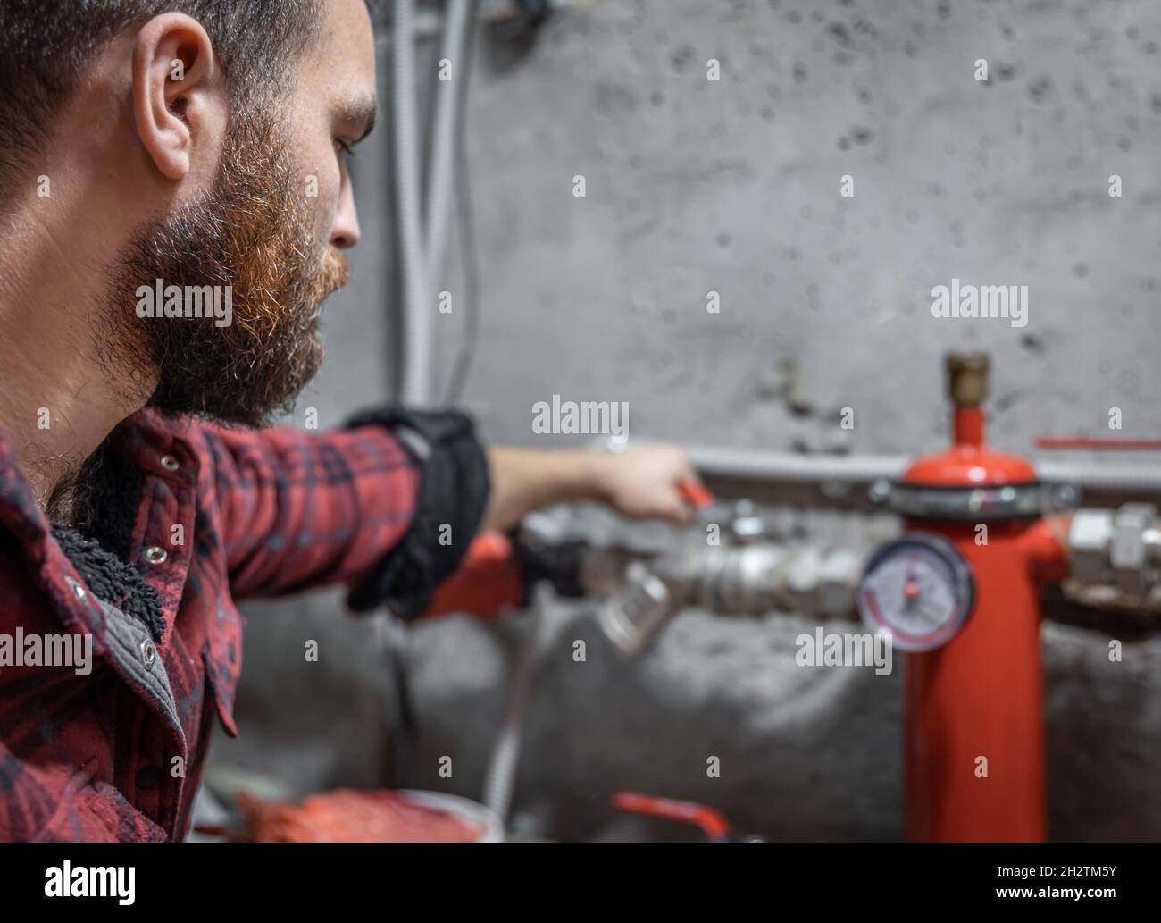 The man looks at the faucet, pipes, valve, pressure meter. Stock Photo