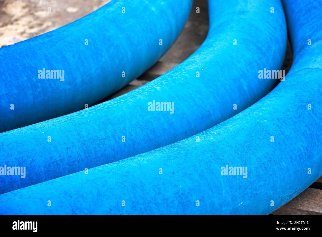 Three curved blue pipes for laying the gas pipeline lie in an open warehouse on the street. Layout. Products for the construction of the gas pipeline. Stock Photo