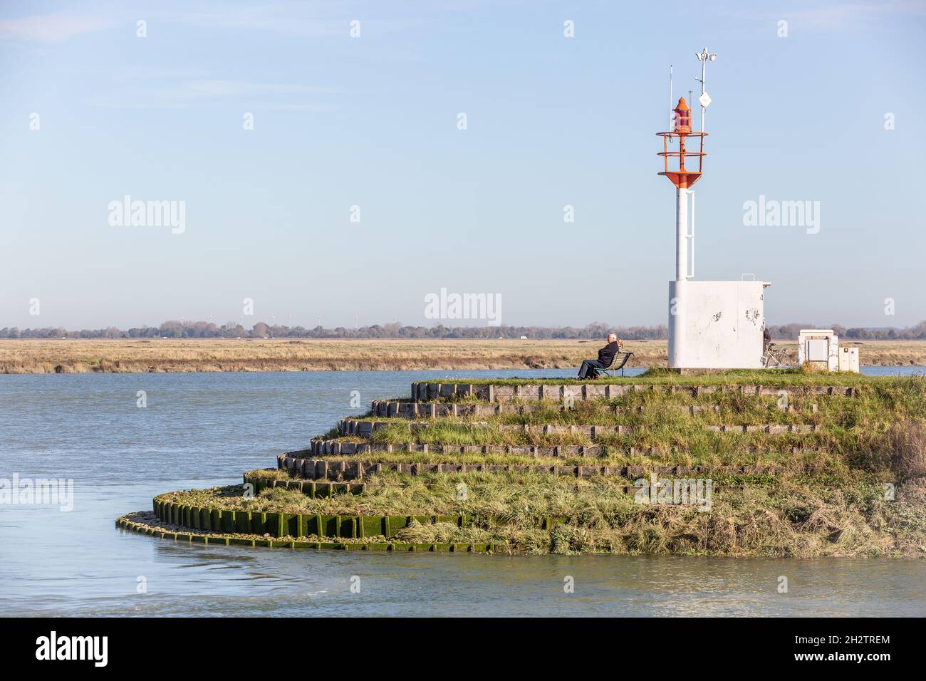 Beacon marking access to the port of Saint-Valery, man sitting on bench. Bay of Somme. France Stock Photo