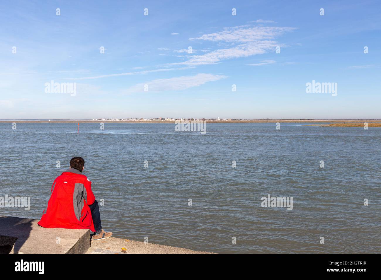 Man in a red coat contemplating the Baie de Somme at high tide. Saint-Valery, France Stock Photo
