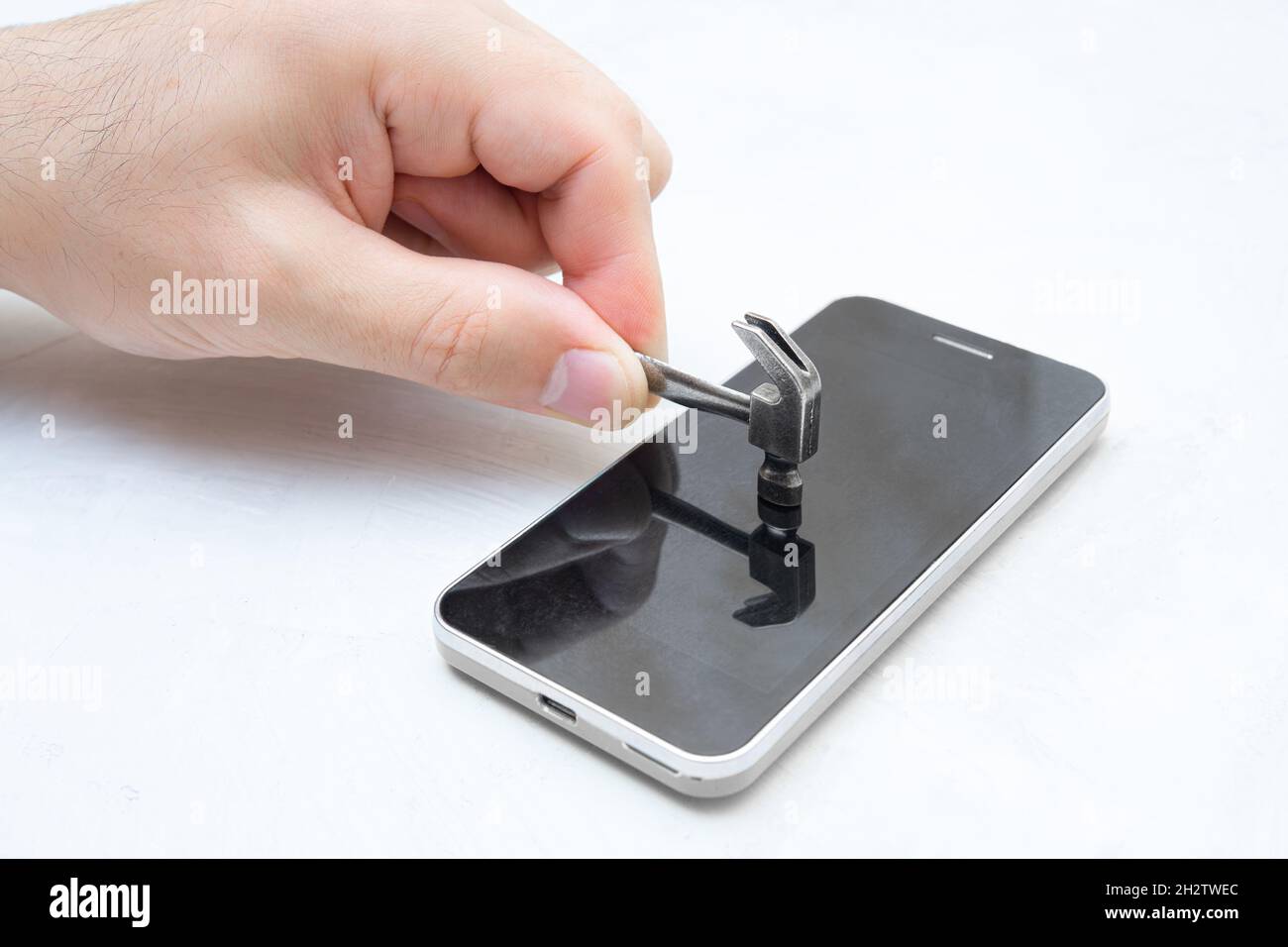 Hand hitting the screen of a mobile phone with a small steel hammer. Stock Photo