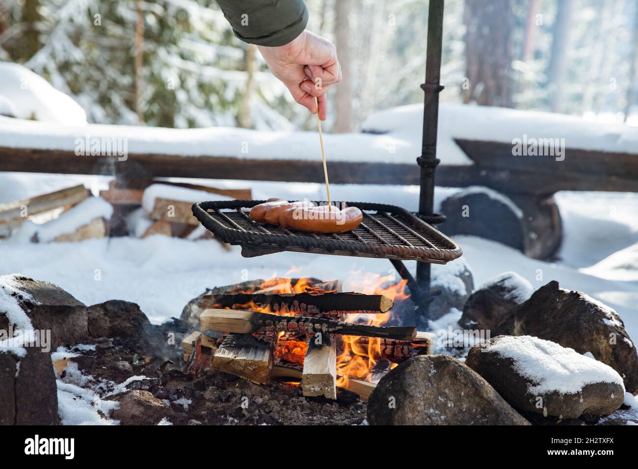 Man roasting sausages on campfire in forest by the lake, making a fire,  grilling. Happy tourist exploring Finland. Beautiful sunny winter landscape  Stock Photo - Alamy