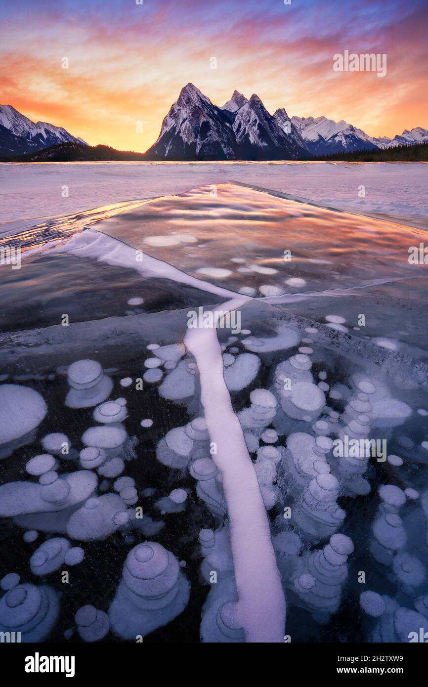 Stunning sunrise with leading ice creacked line and trapped frozen methane bubbles within ice surface, Lake Abraham, Alberta. Winter storm in Canada. Stock Photo