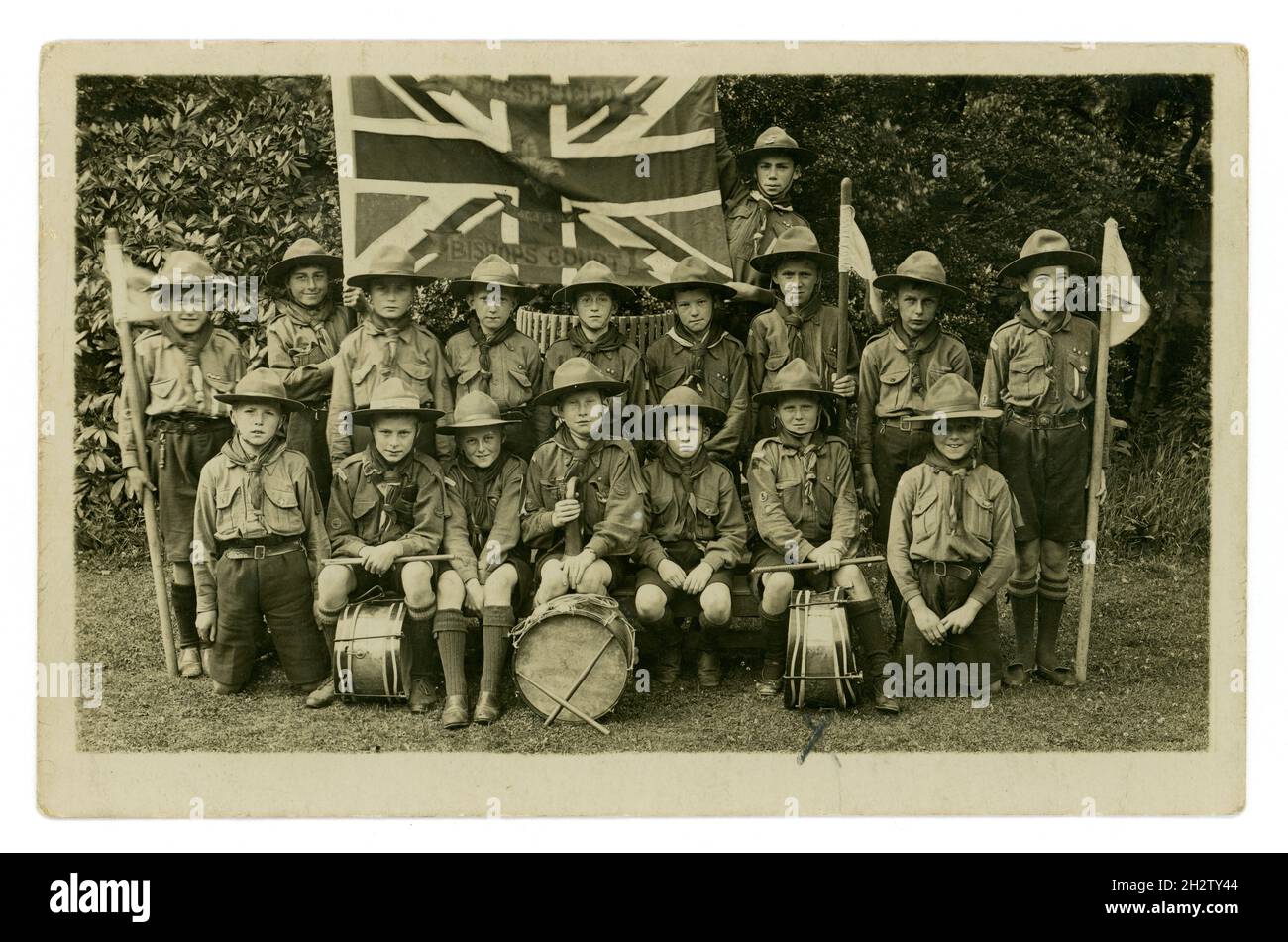 Original early 1900's postcard of 1st Freshfield Bishop’s Court Scout Troop band (founded in 1915), with Union Jack flag with Freshfield, Bishop Court and the Scout motif embroidered  on it. The boys at the front are holding their drums, wearing hats and some are holding flags. Bishop's Court School, Freshfield, Formby, Liverpool, Lancashire, U.K.  circa 1918, 1919 or early 1920's Stock Photo