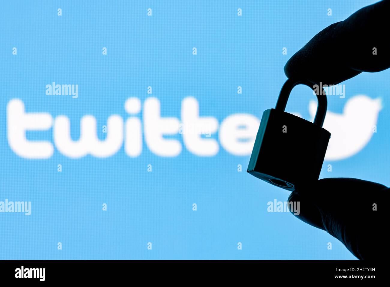 Fingers hold a closed security lock on the background of the Twitter social network logo. The concept of data security in Twitter. Stock Photo