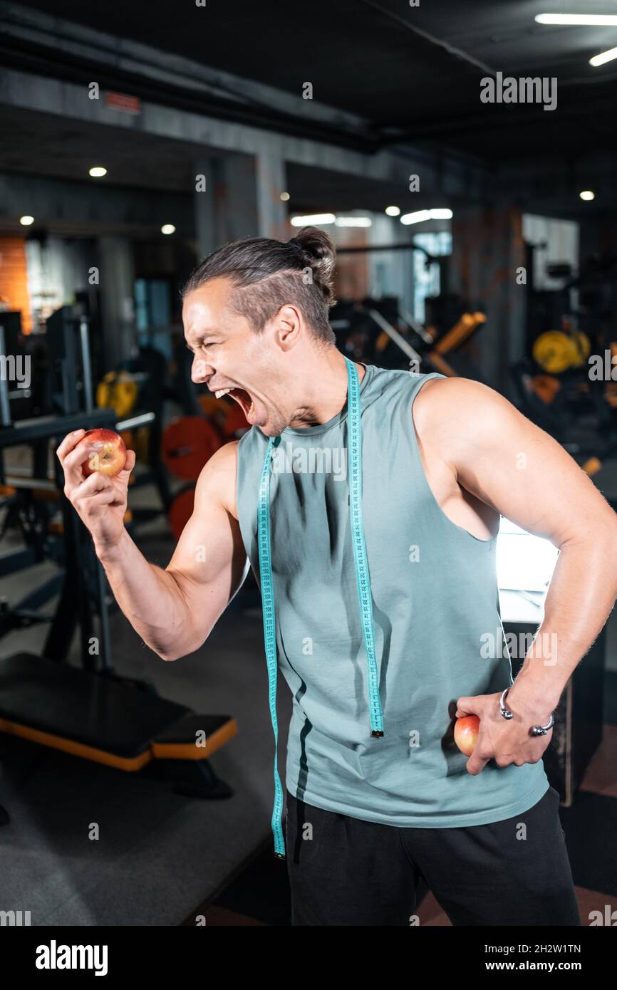 young handsome athlete hungry and eating healthy apple fruit in gym Stock Photo