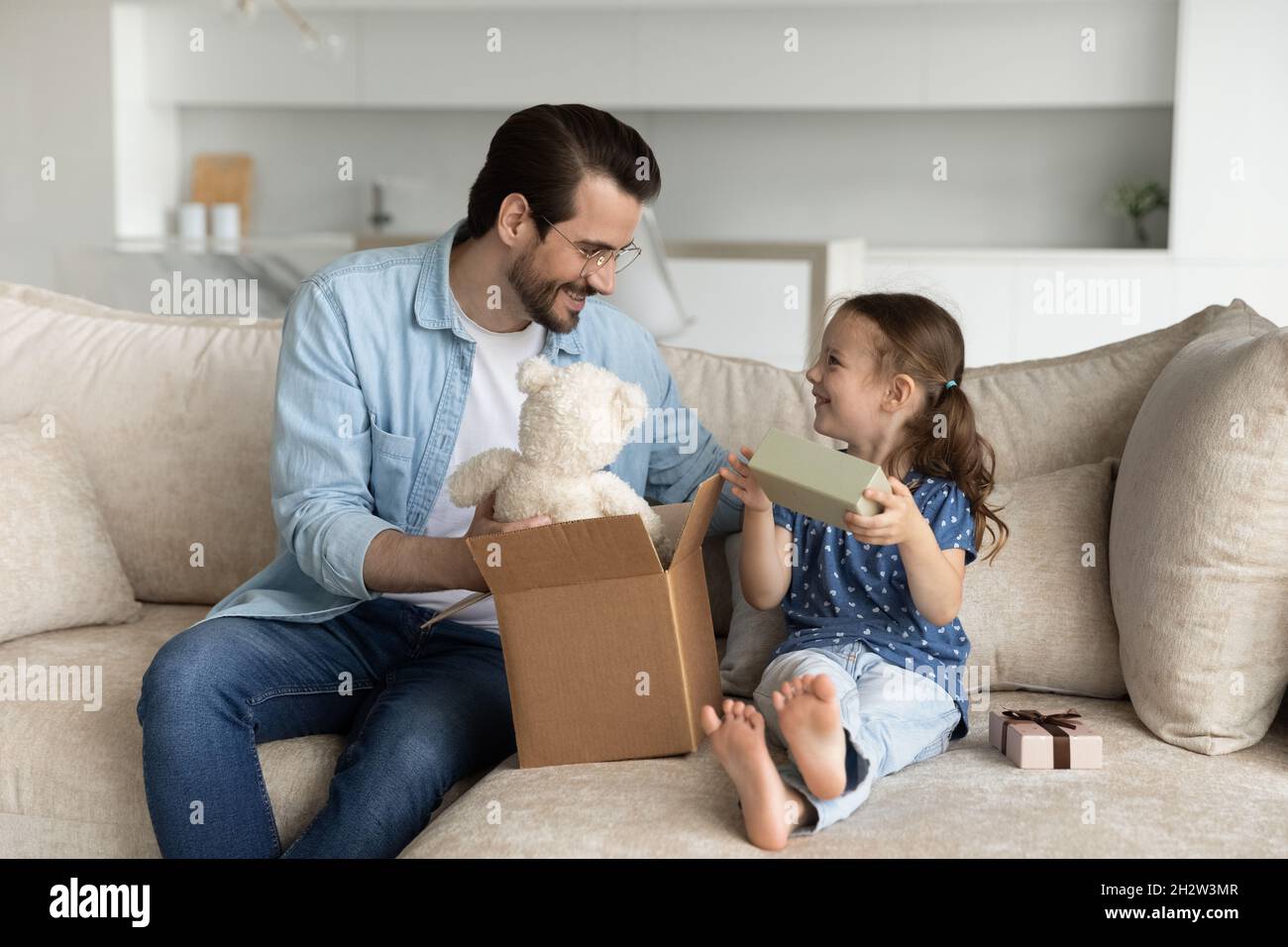Happy young father unboxing parcel with gifts for small daughter. Stock Photo