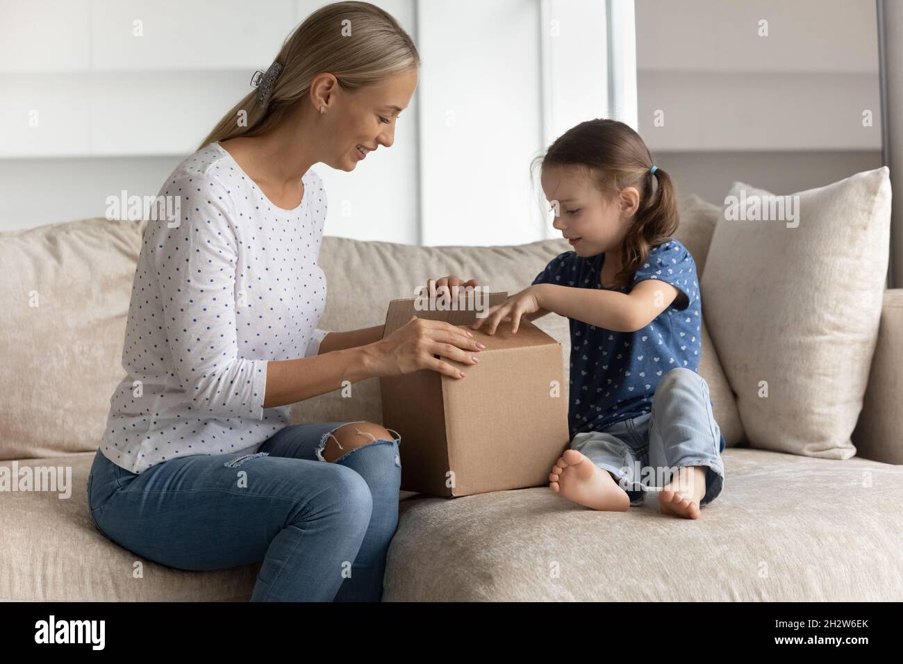 Happy young mother unpacking box with little kid daughter. Stock Photo