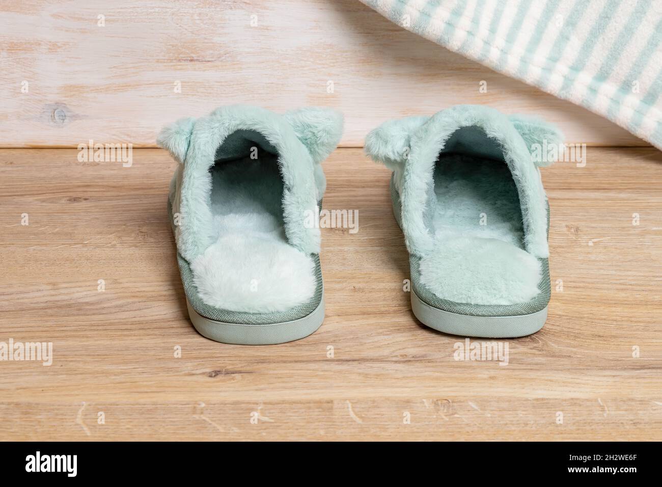 Blue soft fleece cozy slippers on the brown floor in the bedroom. Funny domestic shoes for cold winter season close-up. Warm indoors footwear. Stock Photo
