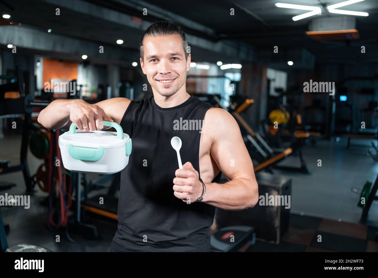 young attractive man personal trainer holding lunch box with breakfast in gym Stock Photo