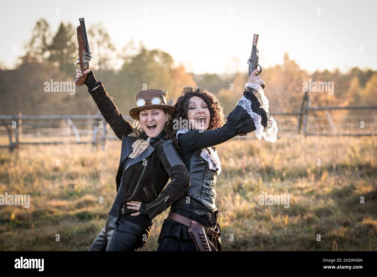 Two women in steampunk costumes with fake pistols rejoice and point gun barrels up Stock Photo
