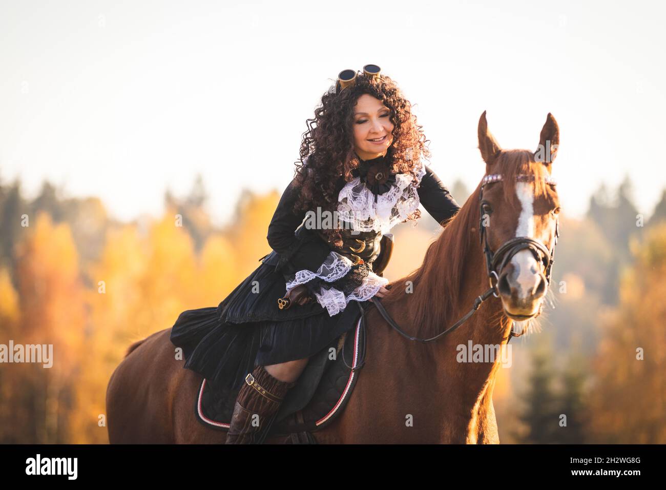 Portrait of a mature woman in a steampunk costume on a horse against the backdrop of an autumn landscape. Stock Photo