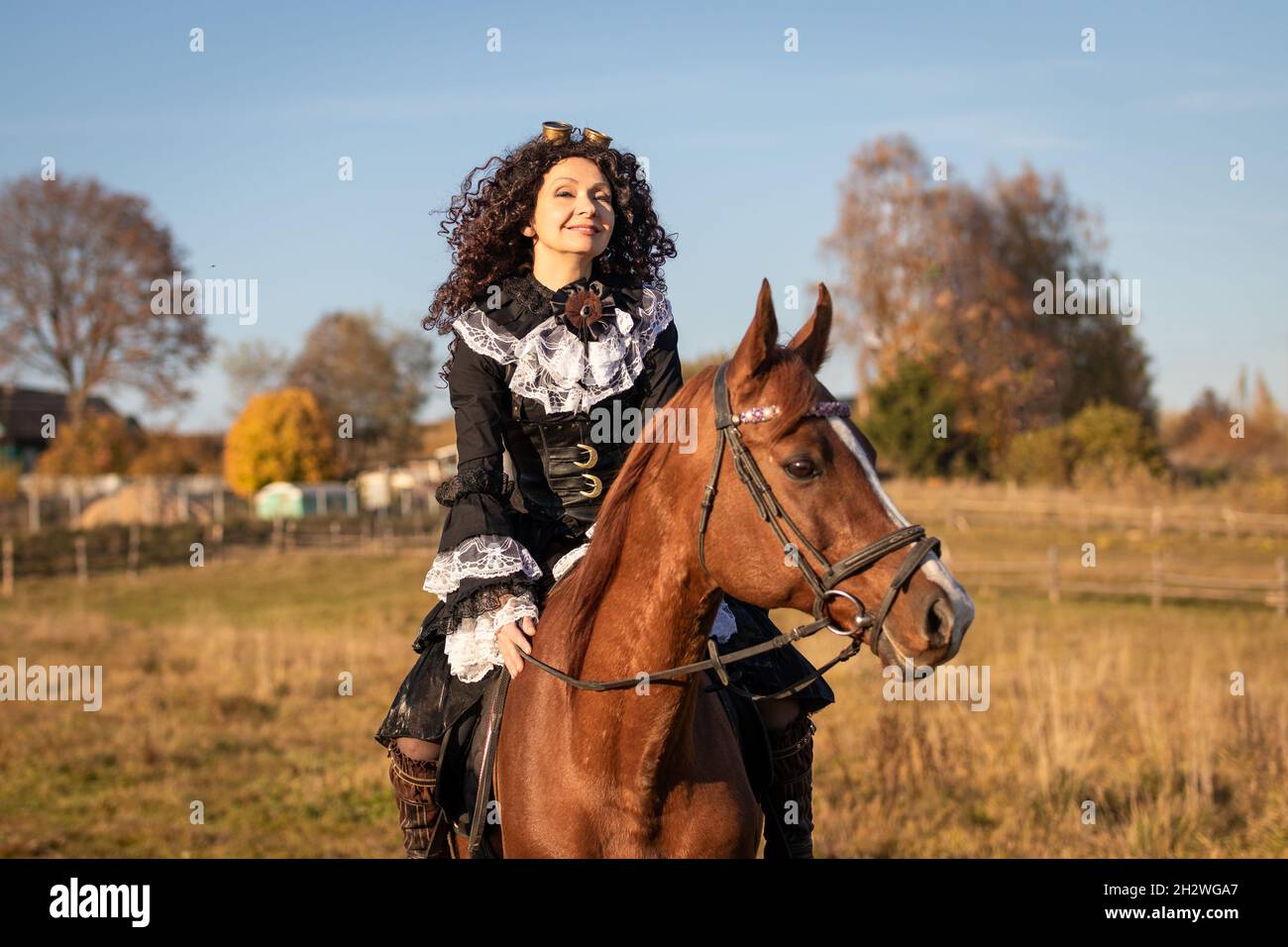 Portrait of a mature woman in a steampunk costume on a horse against the backdrop of an autumn landscape. Stock Photo