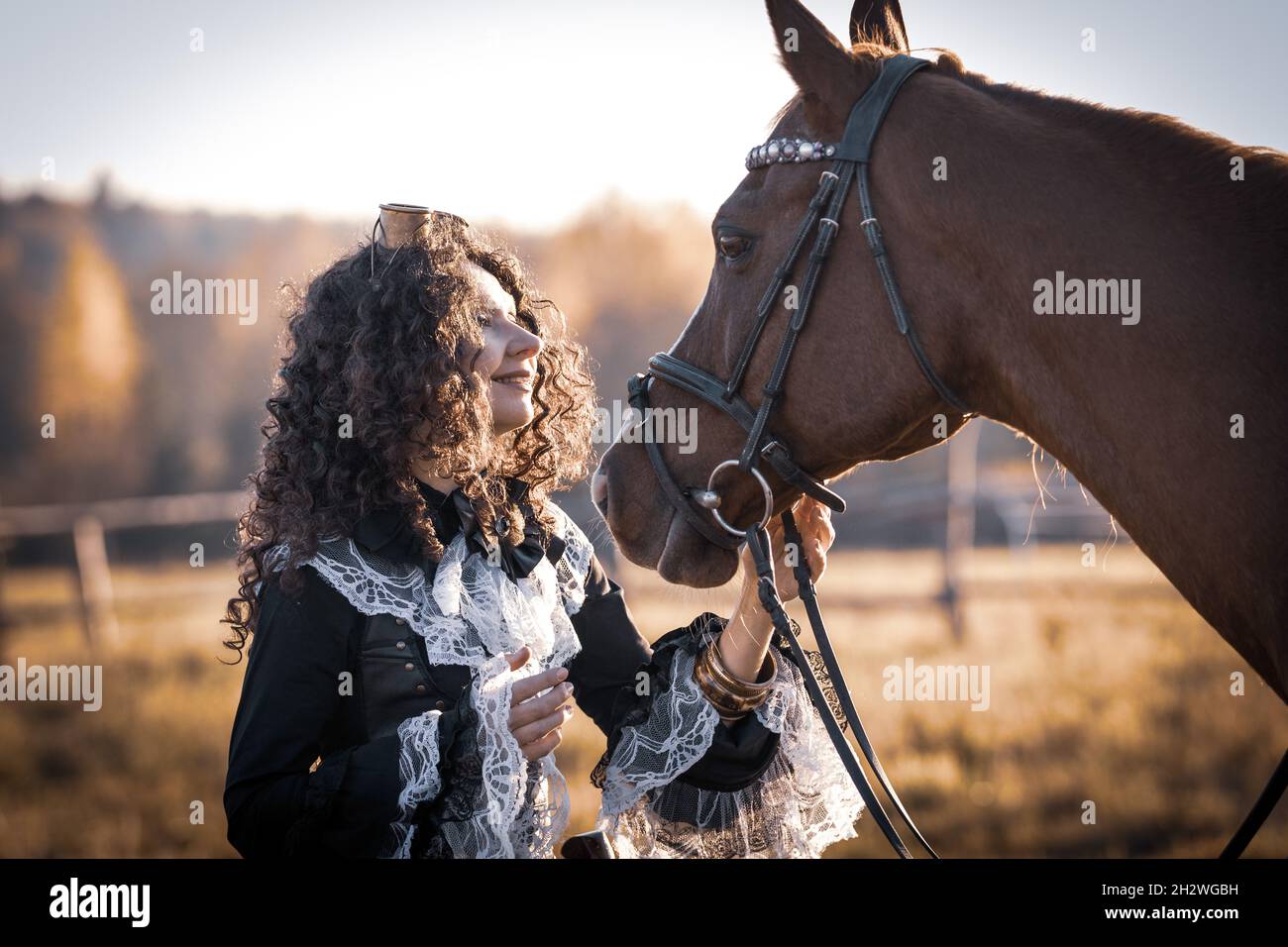 Portrait of a mature woman in a steampunk costume posing with a horse against the backdrop of an autumn landscape. Stock Photo