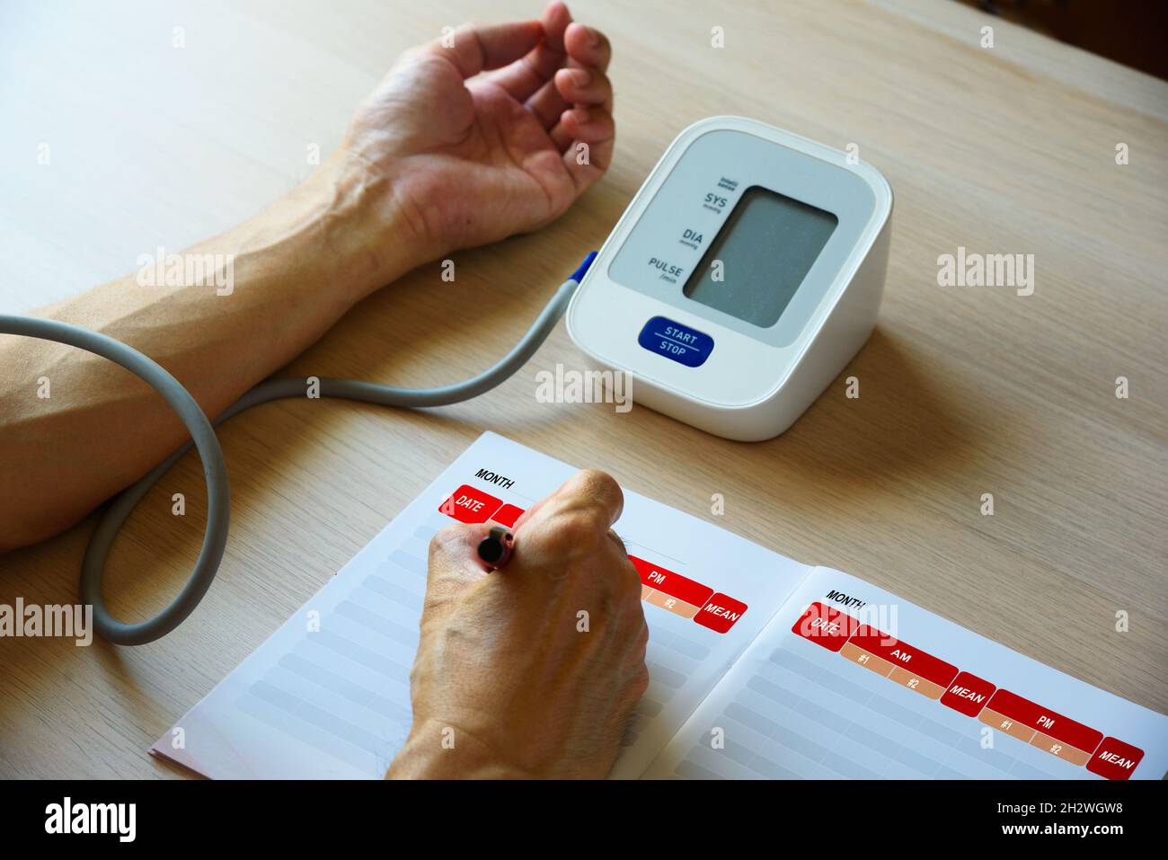 Measuring blood pressure with digital sphygmomanometer at home and recording the number in notebook. Stock Photo