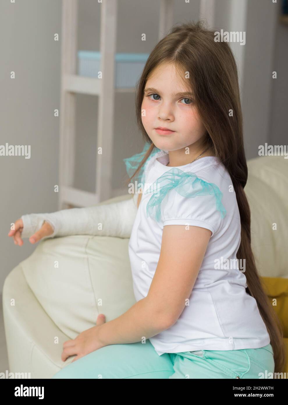 Child with a cast on a broken wrist or arm sits on a couch. Recovery