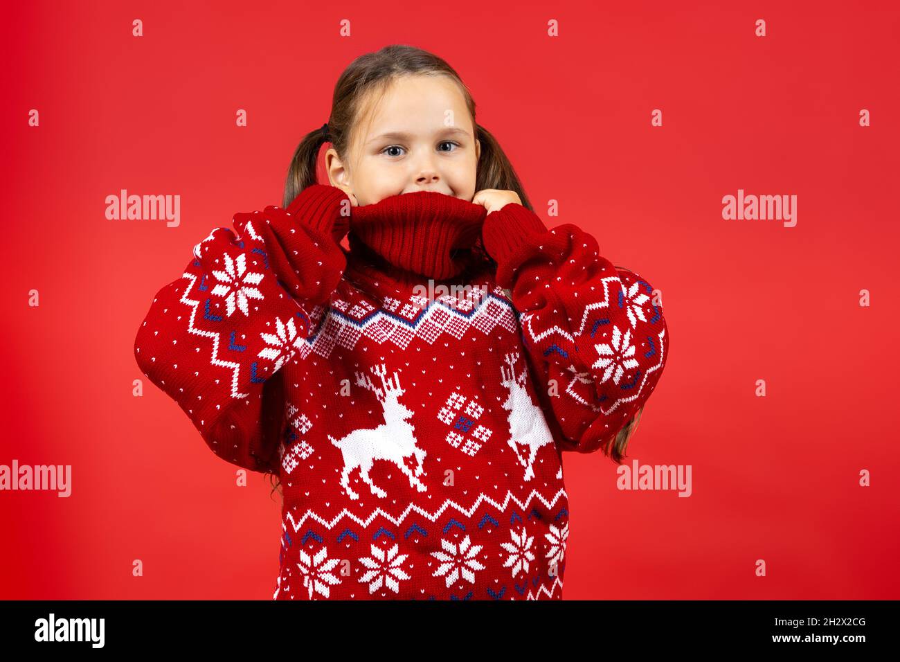 portrait of joyful girl wearing red Christmas sweater with reindeer , isolated on red background Stock Photo