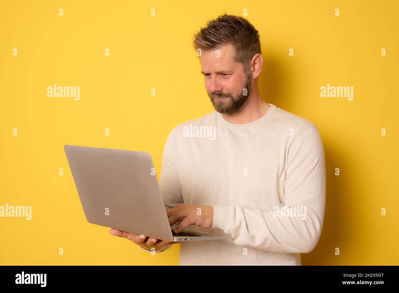 Young handsome man using laptop isolated over yellow background. Stock Photo