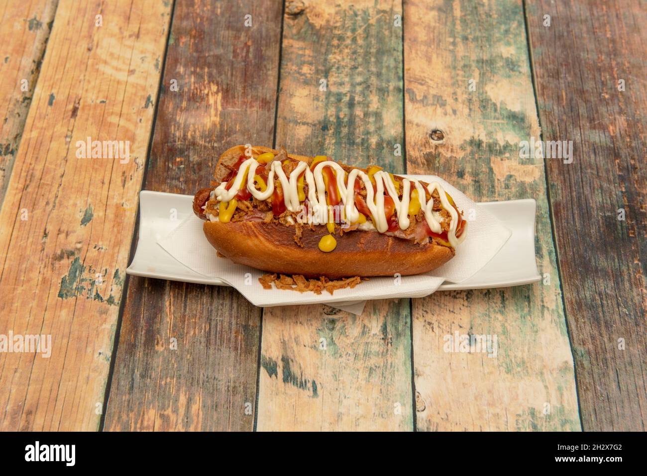 American hot dog with sausage, crispy onion, mustard, ketchup, mayonnaise on white plate Stock