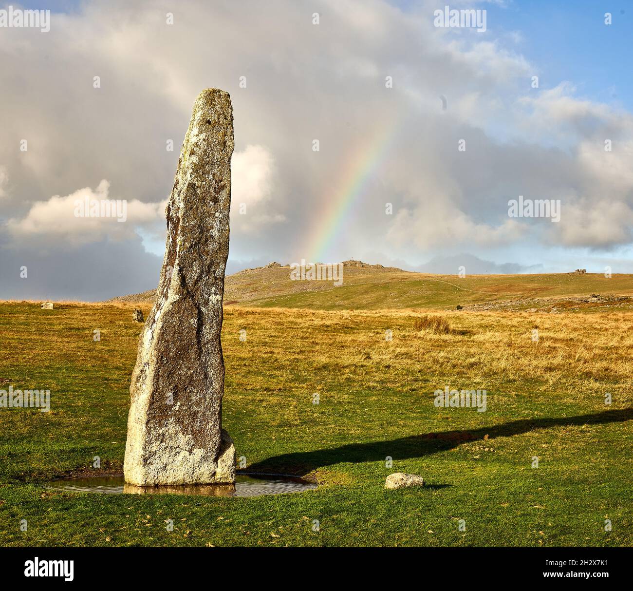 Bronze Age standing stone at Merrivale on Dartmoor Devon UK with Great Mis Tor and rainbow on the horizon Stock Photo