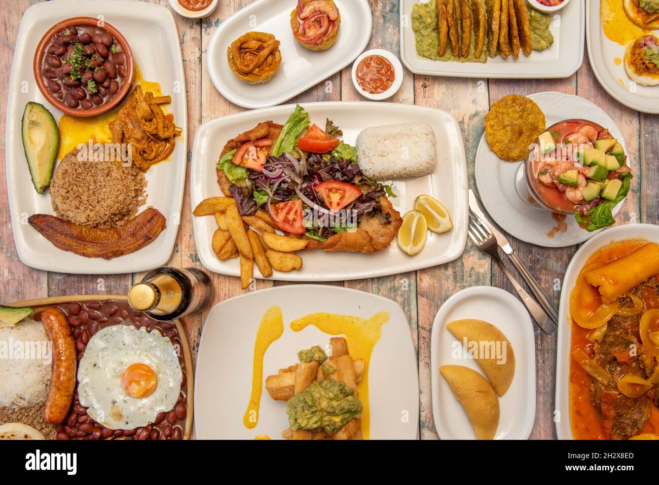 set of delicious Colombian food recipes on wooden table with paisa tray, patacones, chicharrones, fried yucca with guacamole, prawn cocktail and corn Stock Photo