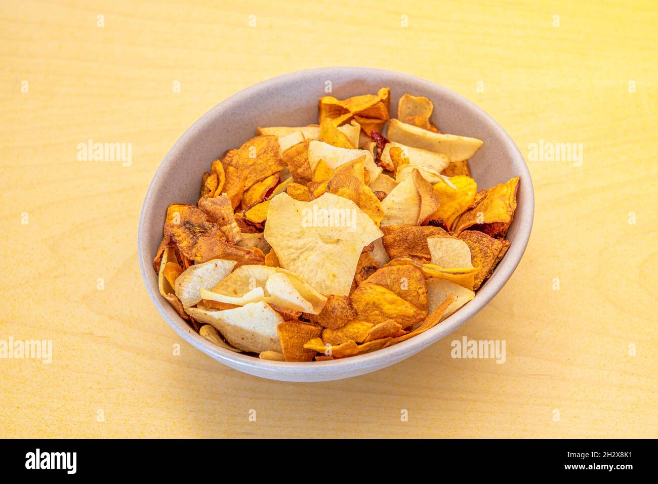 Appetizers bowl of potato chips, sweet potatoes, plantains and other vegetables on yellow table Stock Photo