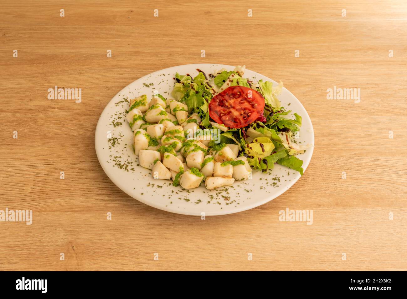 portion of grilled choquito with green sauce and salad garnish with modena vinegar served in a Spanish tapas restaurant Stock Photo