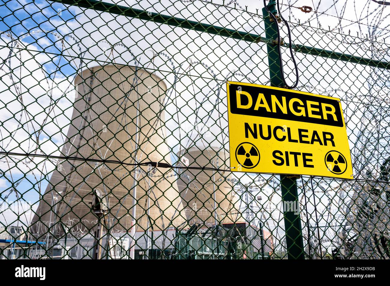 A yellow danger warning sign on the security fence of a nuclear power station with two cooling towers in the background. Stock Photo