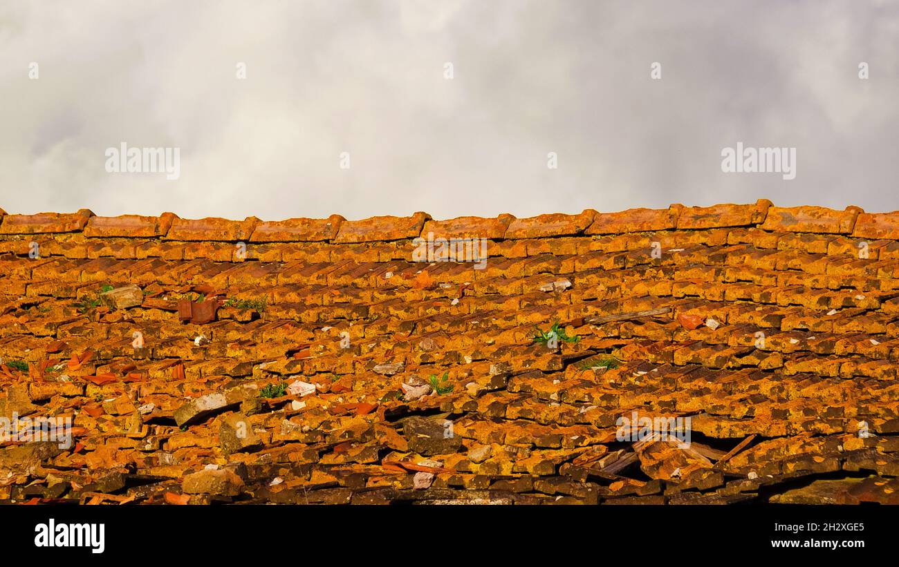 Old and ruined roof tiles with white clouds above as background Stock Photo