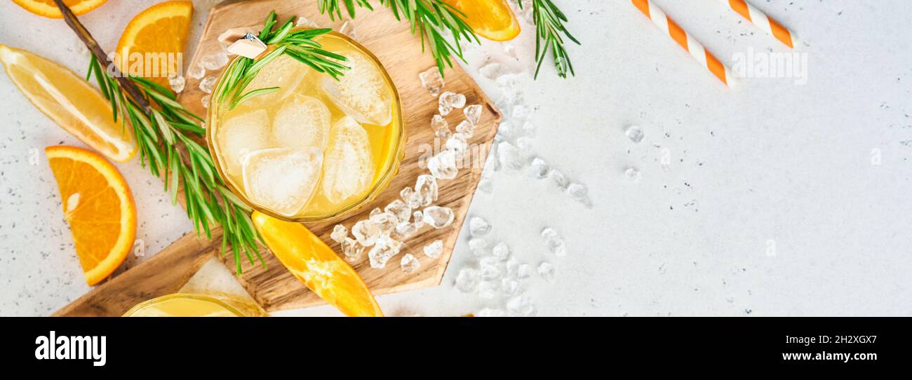 Orange juice or cocktail with rosemary and orange with ice in glass, cold summer lemonade on light gray slate, stone or concrete background. Beach con Stock Photo