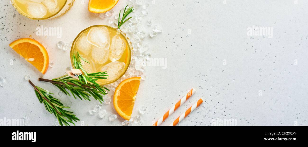 Orange juice or cocktail with rosemary and orange with ice in glass, cold summer lemonade on light gray slate, stone or concrete background. Beach con Stock Photo