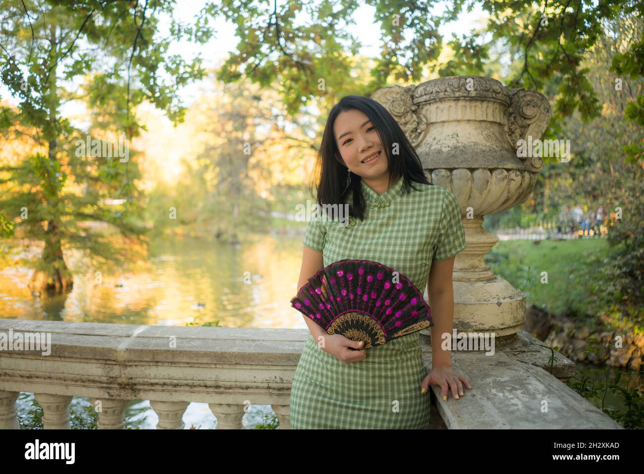 lifestyle portrait of young happy and attractive Asian Chinese woman with traditional fan relaxed taking a walk on city park enjoying Autumn nature du Stock Photo